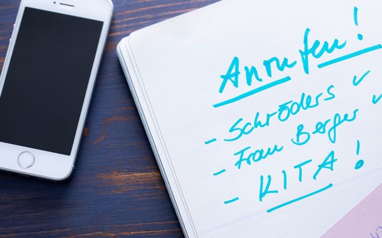 Checkliste für Eltern – Maßnahmen bei Kopfläusen. Notizbuch mit Anrufliste und Smartphone auf einem Holztisch.
