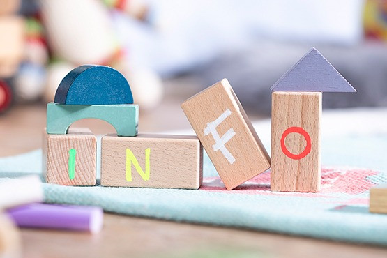 Mehrere bunte Holzbausteine auf einem Teppich, die das Wort „INFO“ bilden. Die Buchstaben sind auf verschiedene geometrische Formen in hellen Farben aufgedruckt. Der Hintergrund ist unscharf.