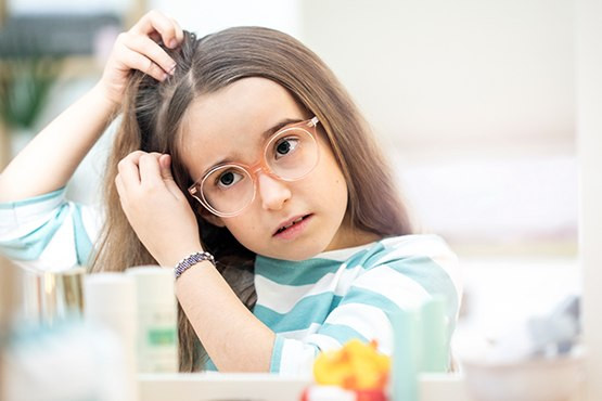 Mädchen mit Brille untersucht sorgenvoll ihren Haaransatz vor dem Spiegel.