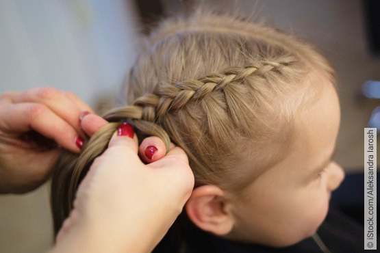 Läuse-Vorbeugung durch Flechten oder Zusammenbinden der Haare bei Kindern. Nahaufnahme von geflochtenen Haaren eines Kindes, während die Haare von einer Person mit roten Fingernägeln geflochten werden.